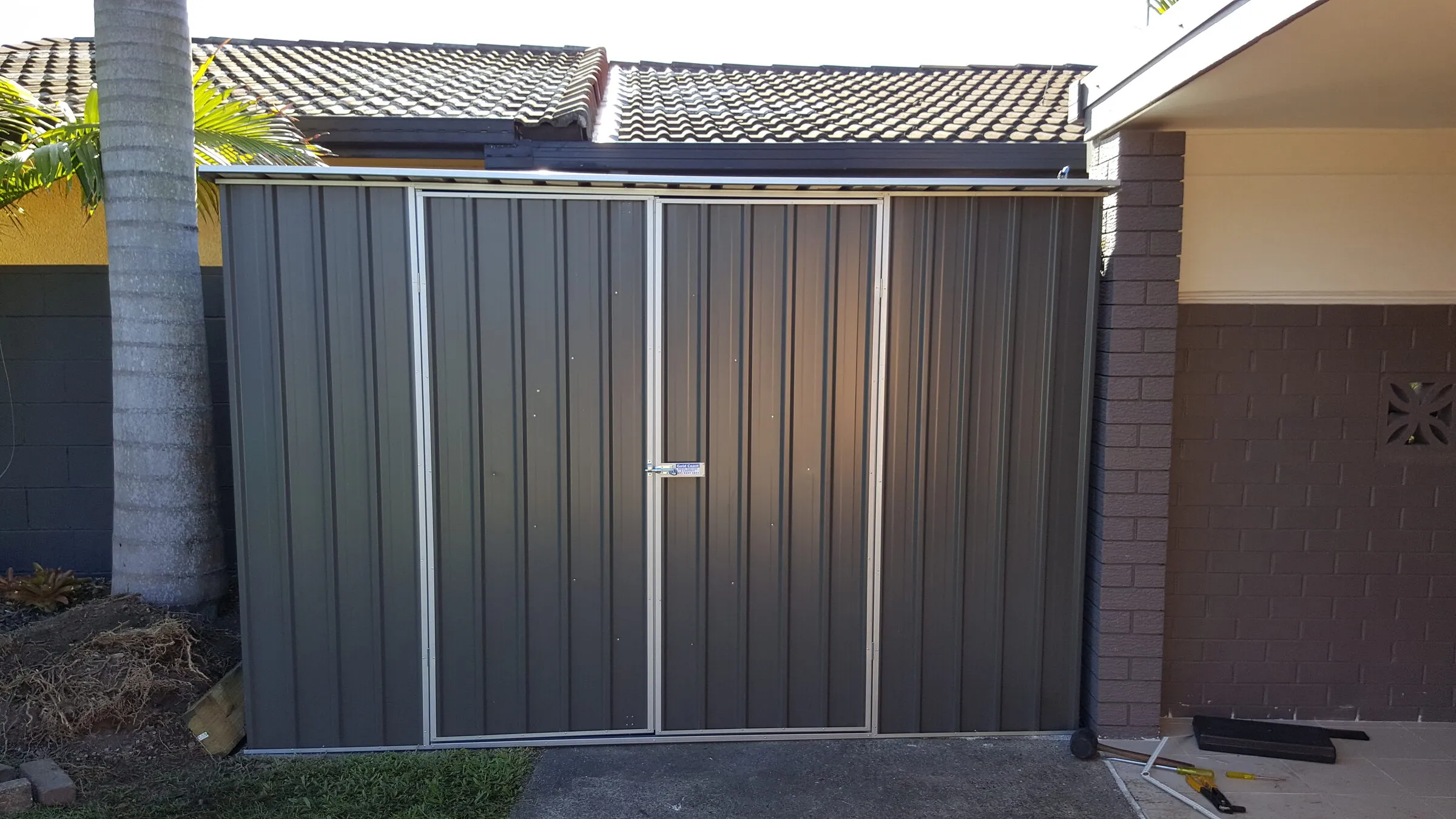A colourbond enclosure with sliding doors built against the side of a house to screen the bins and storage.