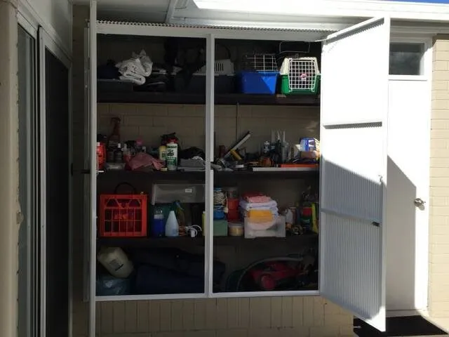 An outdoor storage cupboard with louvre doors, shelved out and in use.