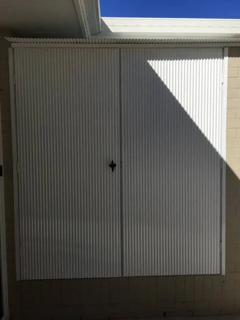 A white corrugated enclosure with double doors closed, built under the eaves to keep the bins out of sight.