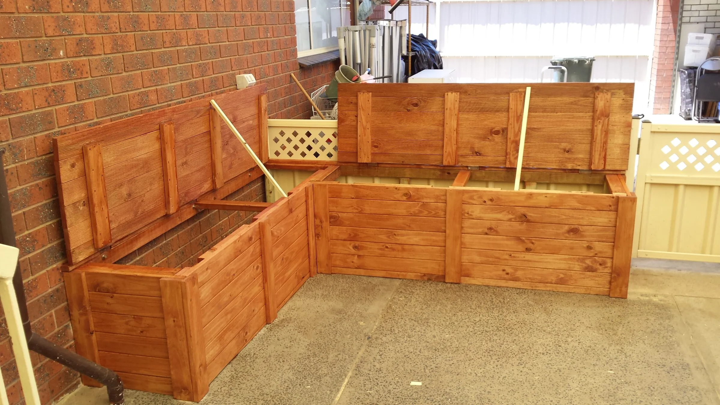 Corner storage benches in stained timber, lids raised, built to fit the return of the wall.