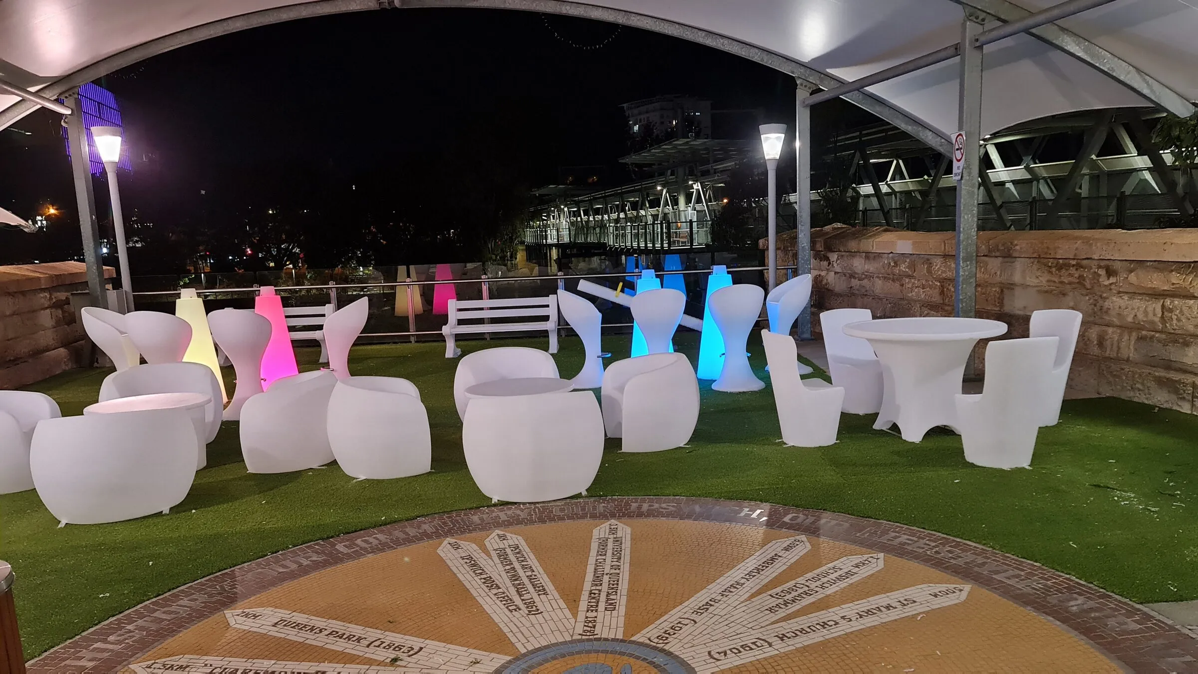 The completed outdoor furniture setting, lit chairs and tables arranged around the mosaic.