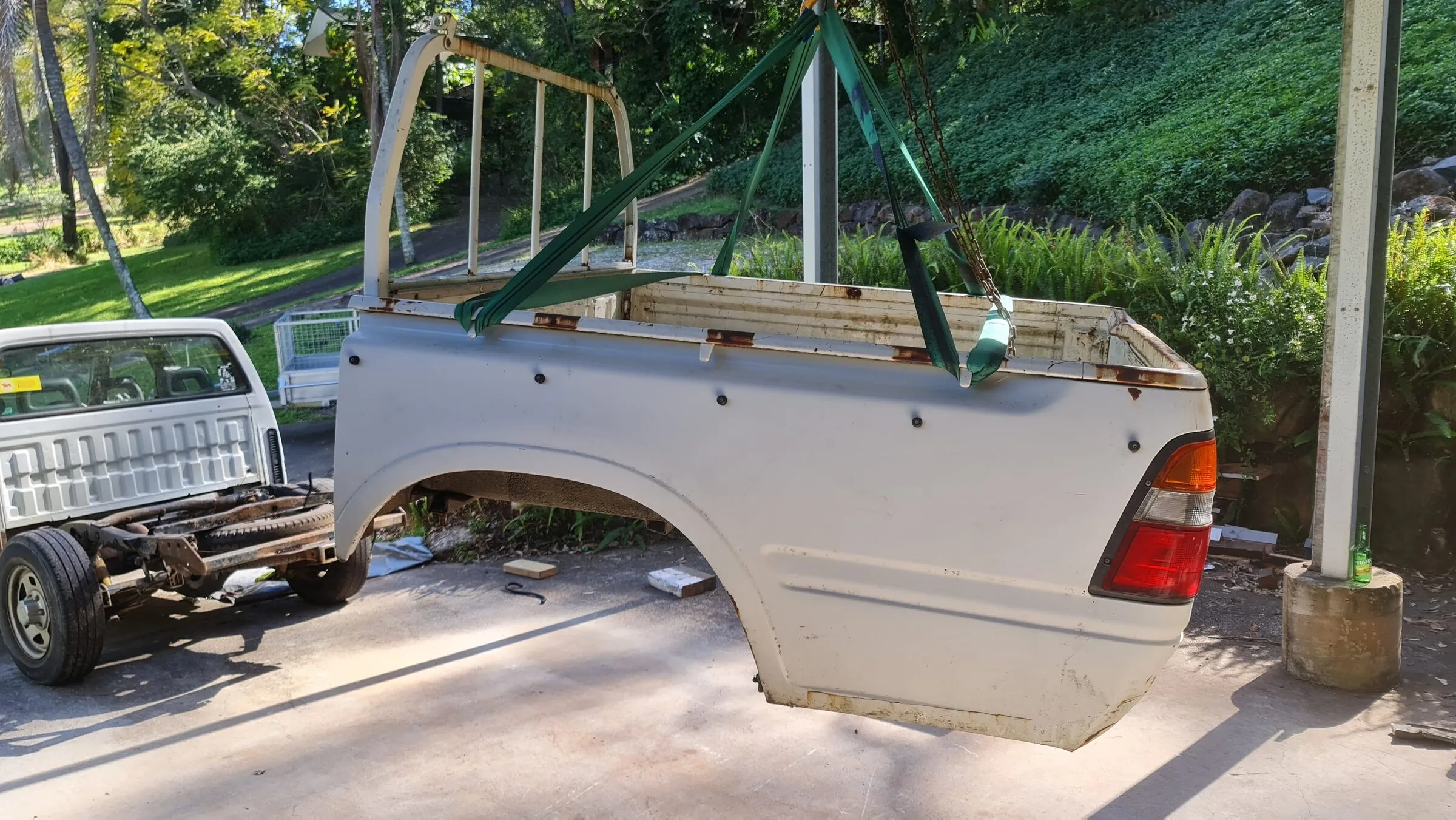 A ute tray lifted clear of the chassis on slings, showing the rusted-out bearers along its underside.