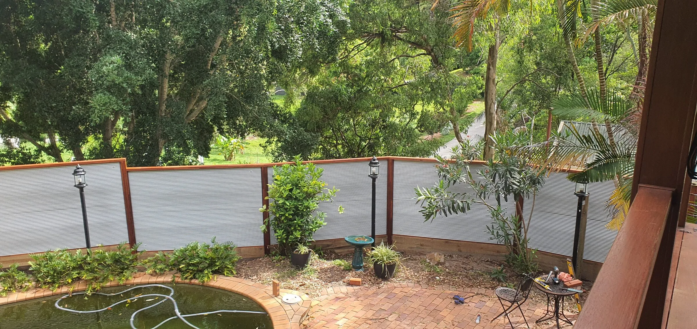 Framed screen panels along a sloping garden boundary, seen from the house across the pond.
