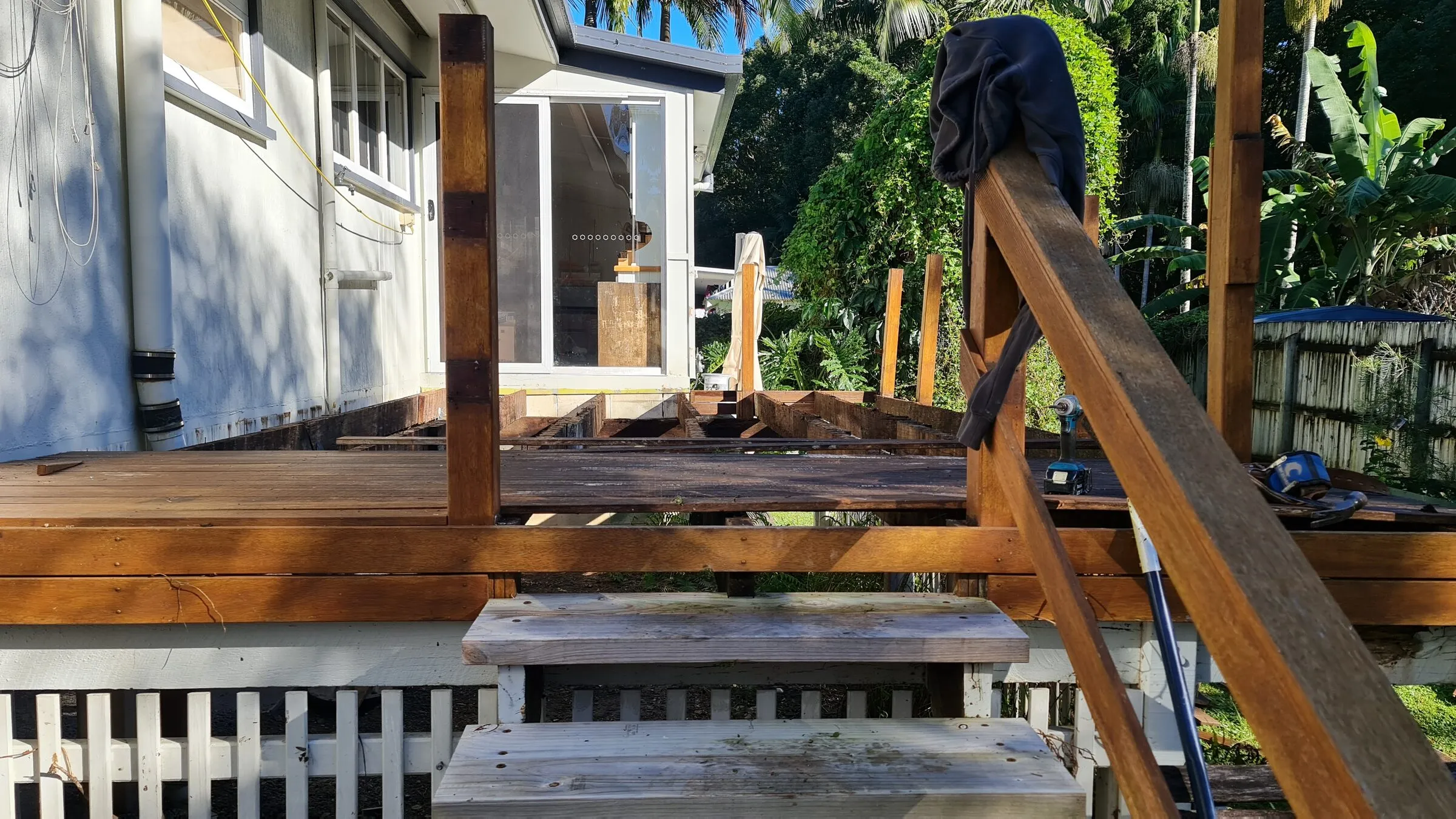 The old deck with its boards lifted, rotted joists showing under the hardwood handrail.