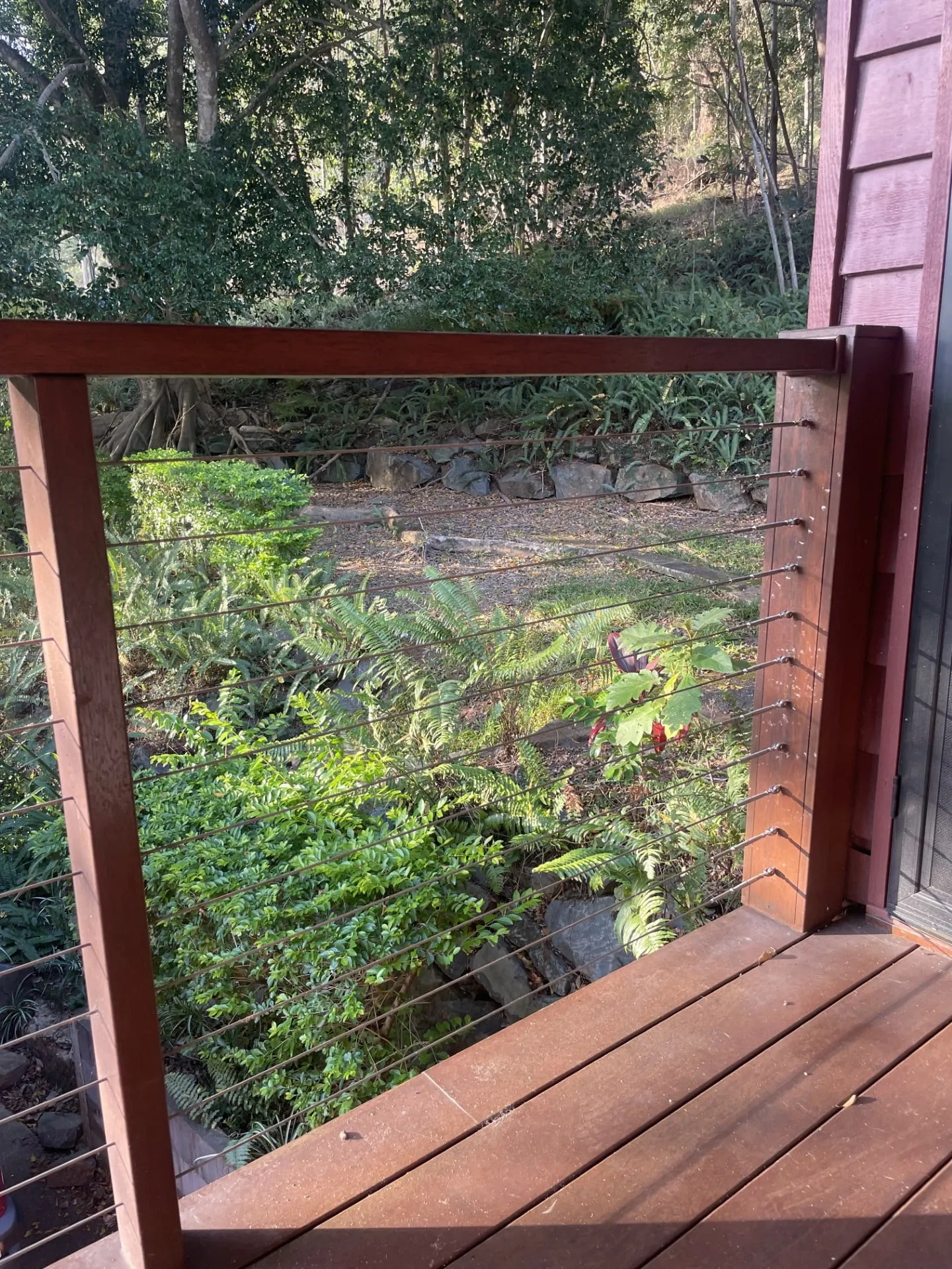 Timber-framed stainless wire balustrade on a deck, bushland behind.